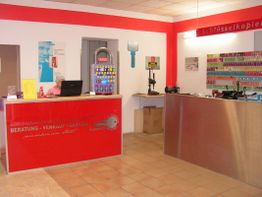 Innenansicht eines Schlüsselgeschäfts mit rotem Tresen und Schlüsselausrüstung an der Wand.