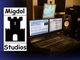 Tonstudio mit Mischpult, Bildschirmen und Lautsprecher neben dem Logo von Migdol Studios.