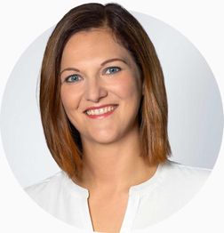 Eine lächelnde Frau mit braunem Haar und weißer Bluse vor weißem Hintergrund.