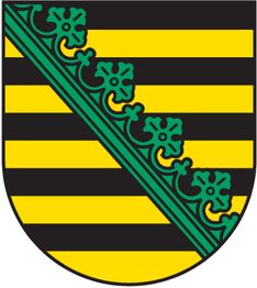 Wappen mit schwarzen und goldenen Streifen und grünem Rautenmuster mit Kleeblättern.