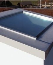 Flachdach mit Lichtkuppel, umgeben von Kies und Dachbegrünung, mit Geländer im Hintergrund.