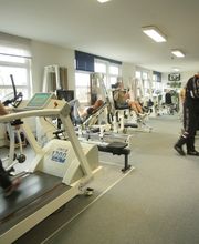 Personen trainieren in einem Fitnessstudio, auf Laufbändern und an Fitnessgeräten.