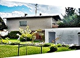 Zweistöckiges Haus mit gepflegtem Garten, Bäumen und bewölktem Himmel im Hintergrund.