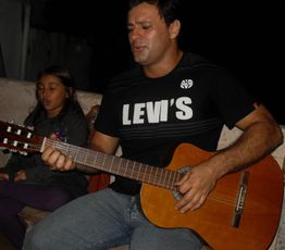 Homem tocando violão enquanto uma menina canta ao seu lado, ambos em um ambiente descontraído.