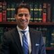Man in a suit smiling in front of a bookshelf with legal books.