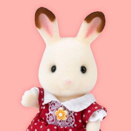 Coelho de pelúcia com vestido vermelho de bolinhas brancas e flor amarela. Fundo rosa.