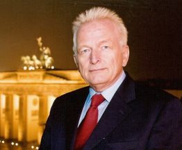 Eine Person im Anzug vor dem nachts beleuchteten Brandenburger Tor.