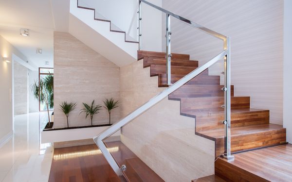 Eine Treppe in einem modernen hellen Flur, mit einem Plexiglasgeländer eingefasst in gebürstetem Metall.