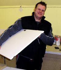 Ein Mann mit dunklem Pullover hält eine weiße Tür in einem Raum mit gelber Wand.