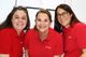 Drei Frauen in roten Poloshirts lächeln in die Kamera.