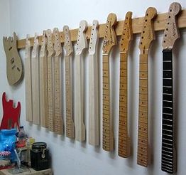 Gitarrenhälse hängen an einer Wand, daneben Gitarrenkörper und Werkzeuge auf einer Werkbank.