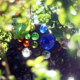 Garrafas coloridas em um jardim cercado por folhas verdes brilhando sob a luz do sol.