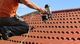Worker using a nail gun on a red tiled roof under a blue sky.