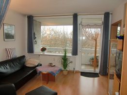 Wohnzimmer mit schwarzem Sofa, Couchtisch, Balkon mit Glastür und Pflanzen.