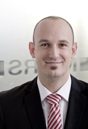 Mann im Anzug mit rot-weiß gestreifter Krawatte lächelt und schaut direkt in die Kamera.