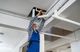 Worker in blue overalls repairing ceiling pipes with tools.
