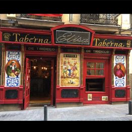 Fachada de una taberna tradicional con puerta y ventanas rojas, decorada con mosaicos.