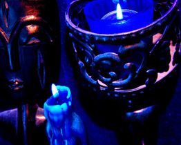 Zwei blaue Kerzen und eine dunkelblaue Maske in geheimnisvollem Licht.