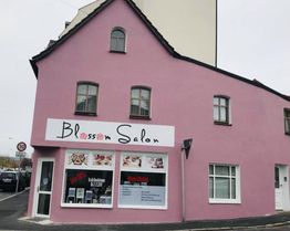 Rosa Gebäude mit "Blossom Salon"-Schild, Fenster und Hinweisschilder, an Straßenecke.