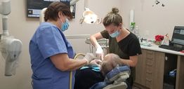 Two dental professionals in masks attending to a patient in a dental chair.