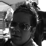 Eine Person mit Sonnenbrille, im Schatten sitzend, schwarz-weiß Foto.