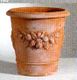 Terrakotta-Blumentopf mit Blumenrelief auf hellem Hintergrund.