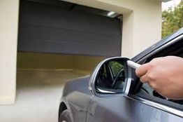 Car with open window, person using remote to open a residential garage door.