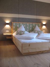 Schlafzimmer mit Holzbett, gestreiftem Kopfteil und zwei Nachttischlampen an grauer Wand.