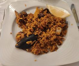 Plato de paella de mariscos con trozo de limón en un plato cuadrado blanco.