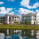 Modern white buildings reflected in a pond under a bright blue sky with fluffy clouds.