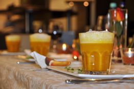 Ein Glas mit gelbem Saft auf einem gedeckten Tisch mit Kerzenlichtern im Hintergrund.