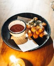 Prato com batatas fritas e molho, sobre mesa de madeira iluminada por vela acesa.