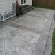 Stamped concrete patio with brick pattern and gravel border next to a white house.