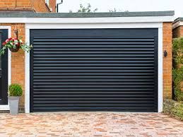 Black garage door with brick walls and potted plants on a paved driveway.