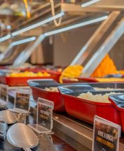 Buffet com várias travessas vermelhas cheias de comida e colheres prateadas ao lado.