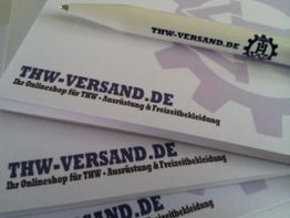 Notizblöcke mit Aufschrift "THW-VERSAND.DE", daneben ein Stift mit gleichem Logo und Text.