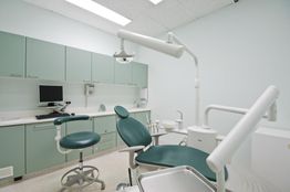 Studio dentistico moderno con poltrona verde, lampada e strumenti odontoiatrici.