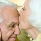 Elderly woman kisses man's forehead, both smiling, showing warmth and affection.