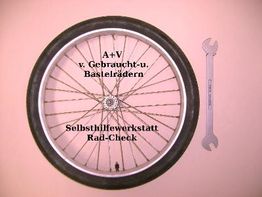 Fahrradreifen mit Aufschrift und ein Schraubenschlüssel an einer rosa Wand.