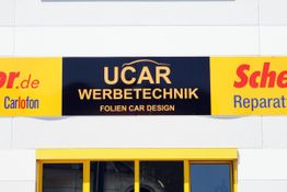 "Ladenschild mit der Aufschrift 'UCAR Werbetechnik Folien Car Design' über einem gelben Eingang."