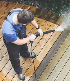Man using a pressure washer on a wooden deck.
