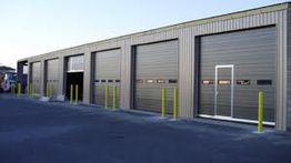 Row of storage units with closed doors and yellow bollards on a clear day.