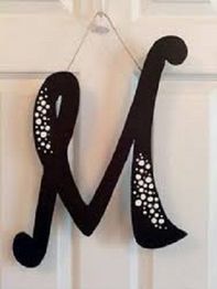 Black wooden letter "M" with decorative holes, hanging on a white door.