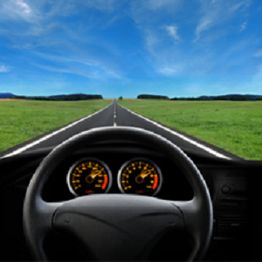 View from car dashboard of an empty road stretching into the horizon under a blue sky.