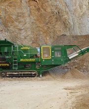 Grüne Baumaschine in einem Steinbruch, umgeben von Steinen und Geröll.