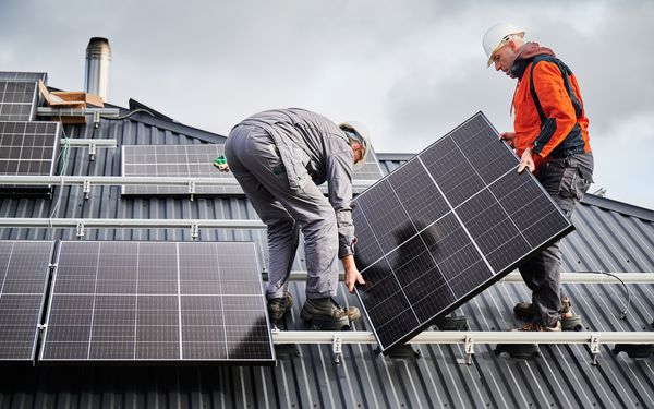 Zwei Solartechniker montieren eine Solarzelle auf dem Dach eines Hauses.