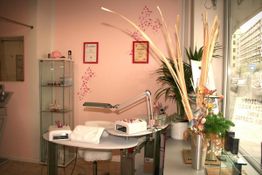 Nagelstudio mit Manikürtisch, Dekoration und Pflanzen, an einer rosa Wand mit Urkunden.