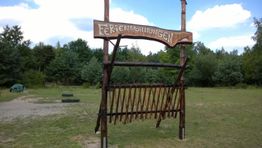 Holztor mit dem Schild "Ferienwohnungen" in einer grünen Landschaft, Bäume im Hintergrund.