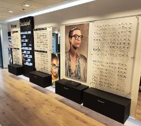Optiekwinkel met brillen op display en grote foto's van gemodelleerde brillen aan de muur.