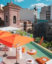 Terraza en la ciudad con sombrillas naranjas y vista a edificios antiguos y modernos.